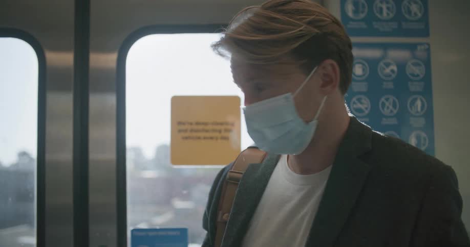 White man wearing a mask using his smartphone next to the train door
