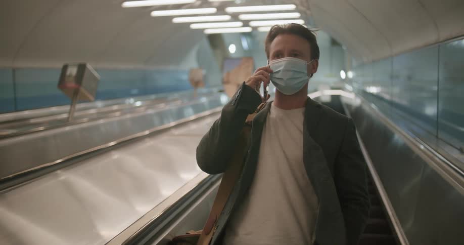 A man riding an escalator down answers his phone