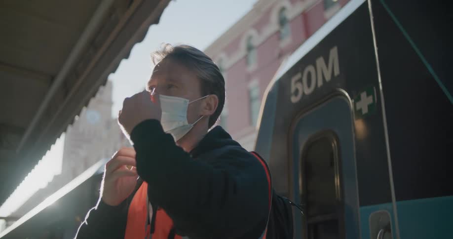 White working man putting a mask on in front of a train