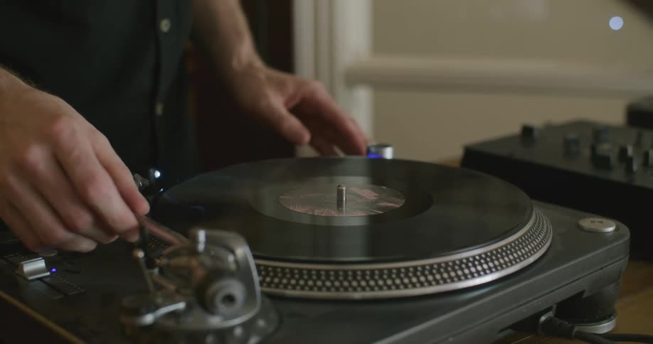 A person places a vinyl record on a turntable and starts playing