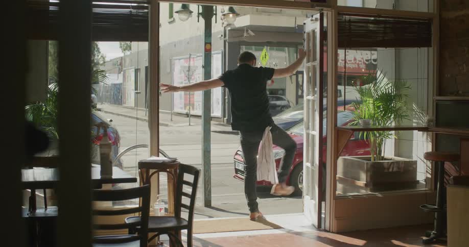 An employee in a restaurant unlocks and opens up the doors as cars and bikes drive past