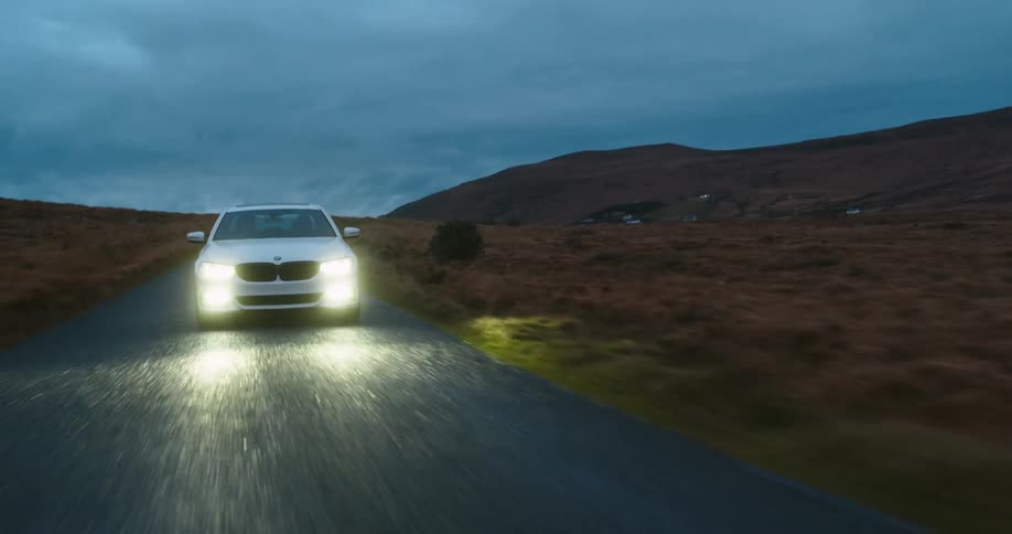 A white car with headlights on driving on a rural road at evening