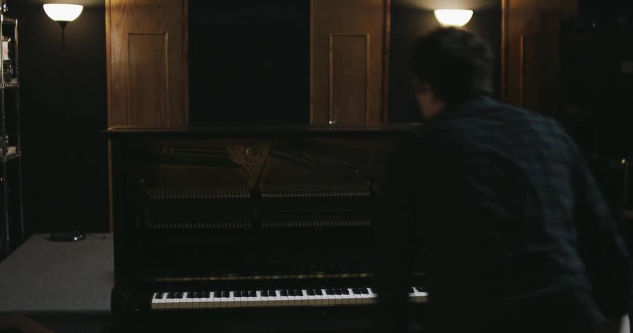A man with a guitar gets up and goes to the piano