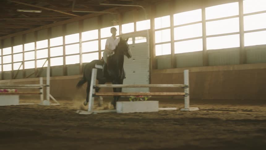 A person rides a horse over jumps in a building