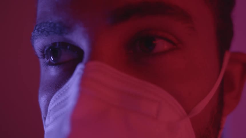 Close up of a young man wearing a face mask in a room under red light