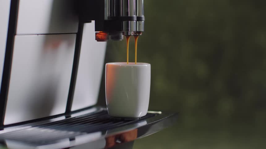A person taking a cup of espresso from an espresso machine