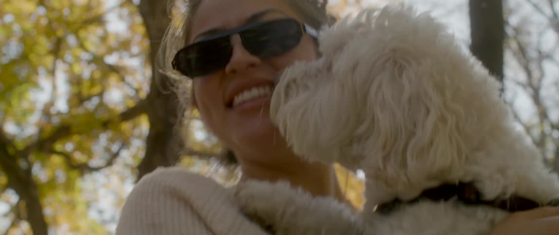 A girl wearing sunglasses holds her dog as she stands outdoors by some trees