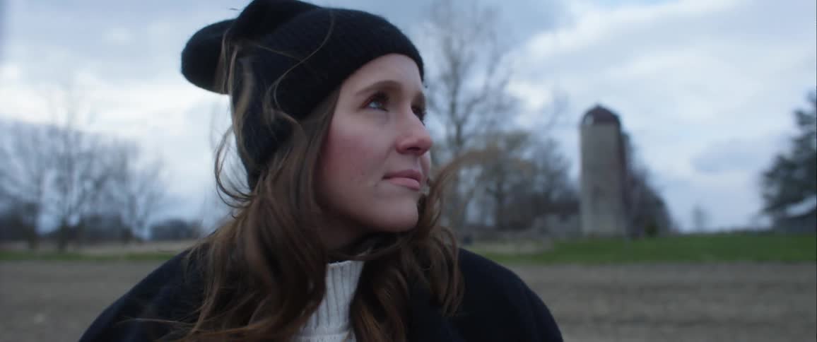 Woman with black beanie and wavy hair looks around on a cloudy day