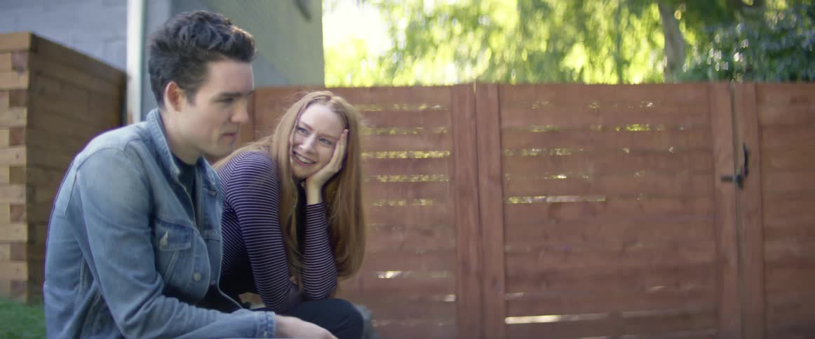A man and woman are sitting in a backyard and talking