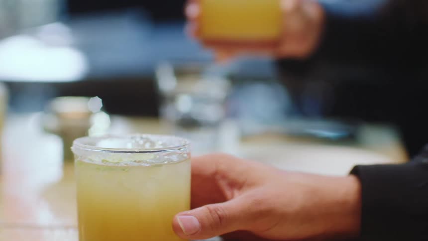 People grabbing yellow cocktail drinks from a table in a restaurant