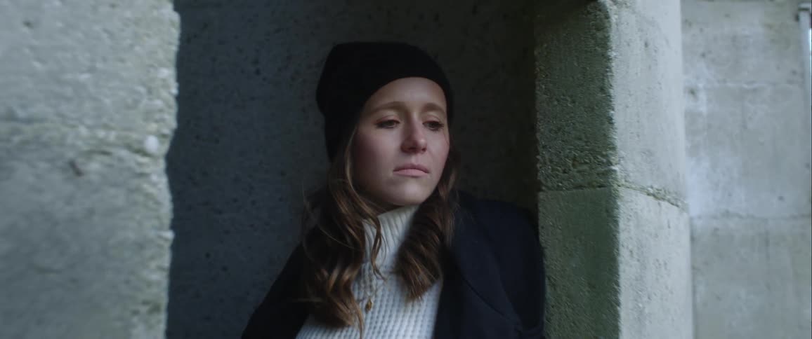 Long haired young woman wearing a white sweater looks sad inside an abandoned building