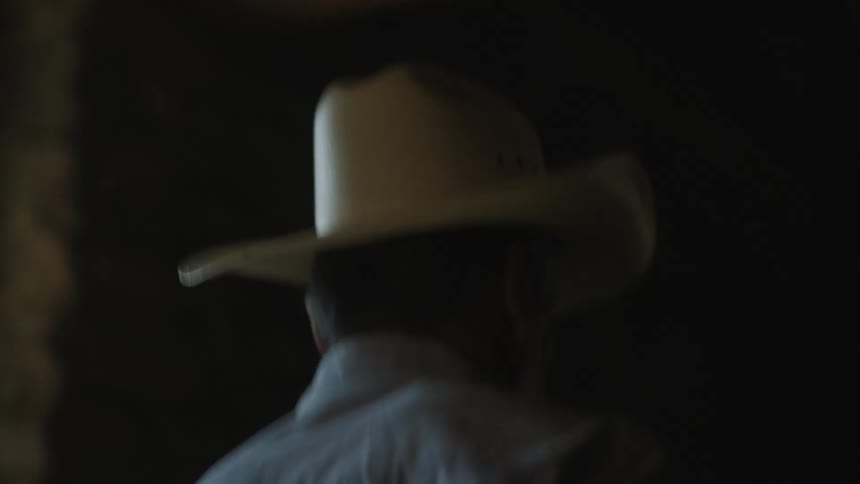 Man wearing a cowboy hat walking on a dimly lit hallway in a ranch
