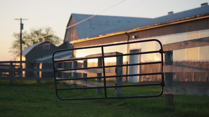 A black metal gate attached to a wooden fence to a stable