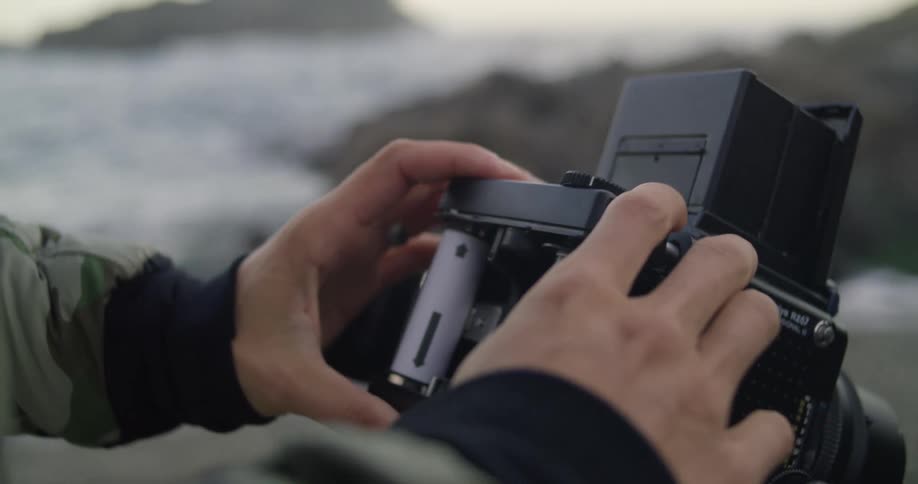 A person putting film into a camera with the ocean sky and clouds in the background