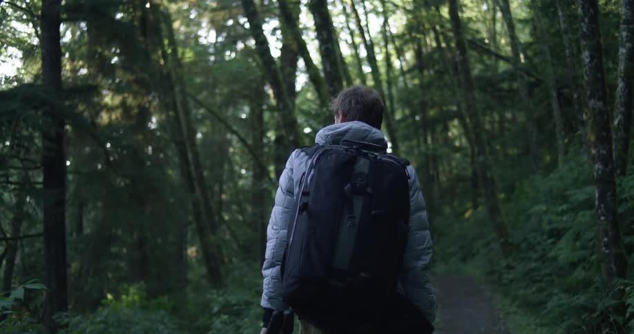 Man wearing a coat and carrying a backpack hiking on a forest path