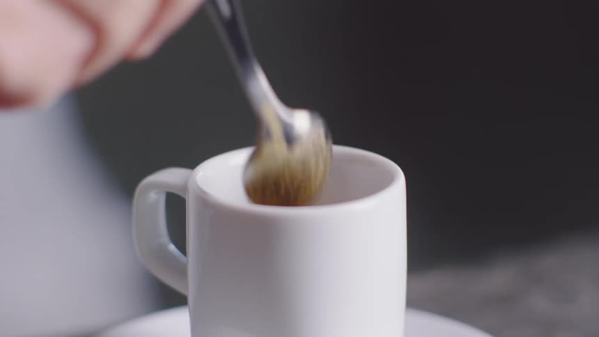 A person stirring a cup of espresso with a spoon and then picking it up