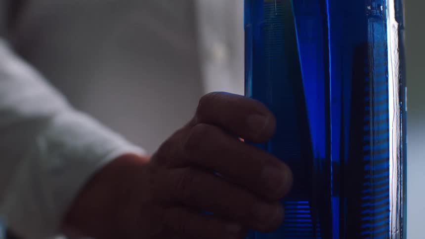 A man submerges a device inside a glass cylinder filled with blue liquid