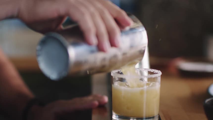 A person pouring an alcoholic drink from a shaker into a glass lined at the top with salt