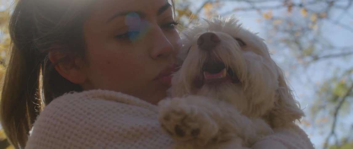 A woman cuddling and kissing her dog under a tree