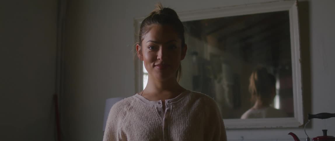 A teenage girl stands with her back to a mirror at home and turns and smiles