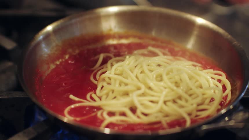 A person puts spaghetti in to a pan of sauce