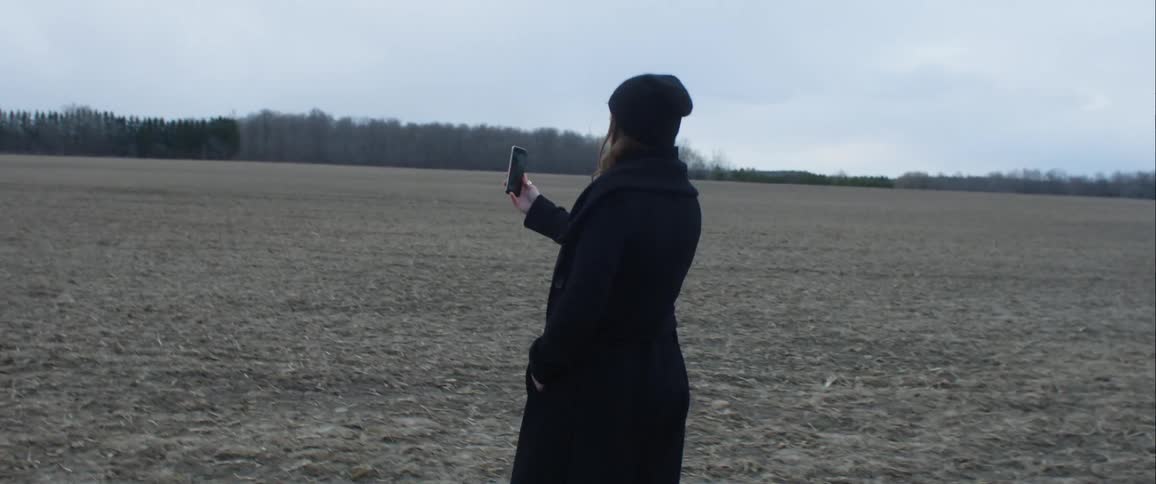Woman wearing winter clothing video calling someone in the middle of a grass field