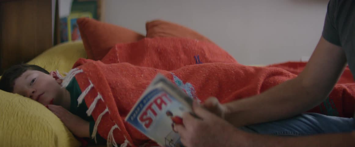 Father tucking son in bed and reading a story