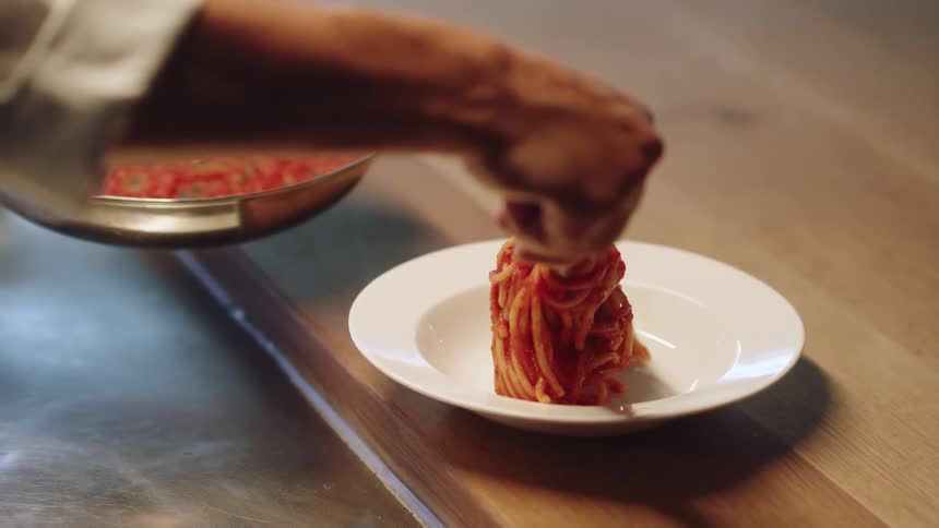 A person is putting spaghetti on a plate