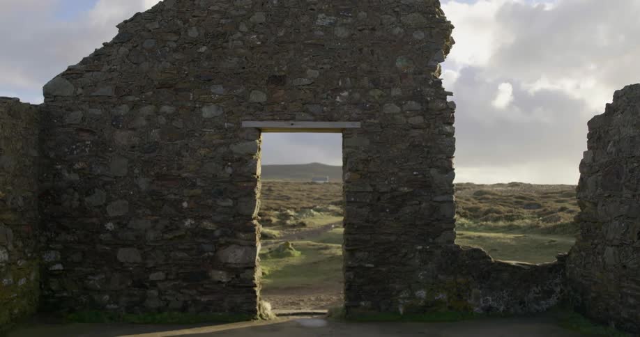 A stone wall with a doorway in front of rolling hills