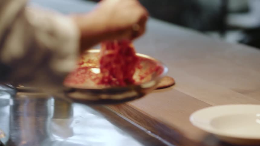 A chef tosses pasta in a pan and brings it over to a counter with an empty white bowl