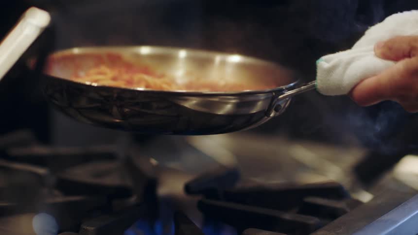 A person is cooking spaghetti in a pan over the oven