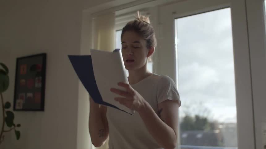 A woman in a room pacing with a book and a pen