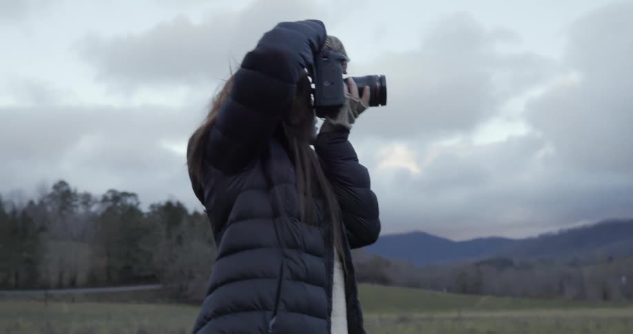 Young woman walking on a grass fields takes pictures of the mountains