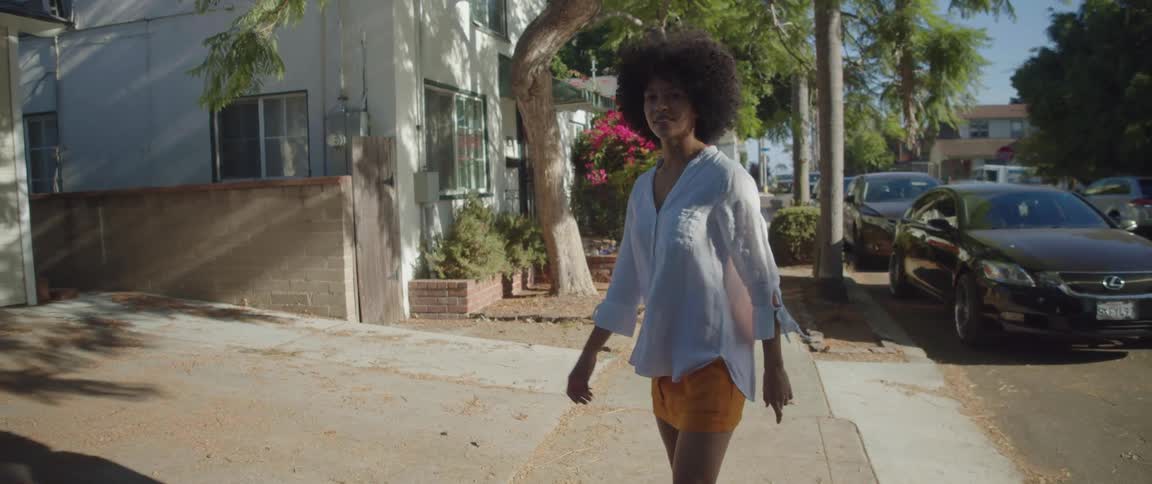 A young black woman with an afro walking down a street with houses spinning in a circle for the camera