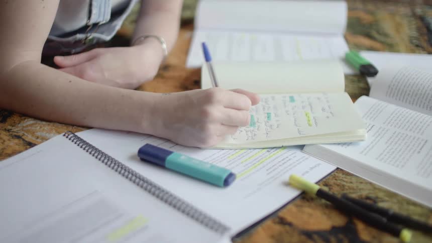 A woman writes in a notebook while lying on a rug doing homework