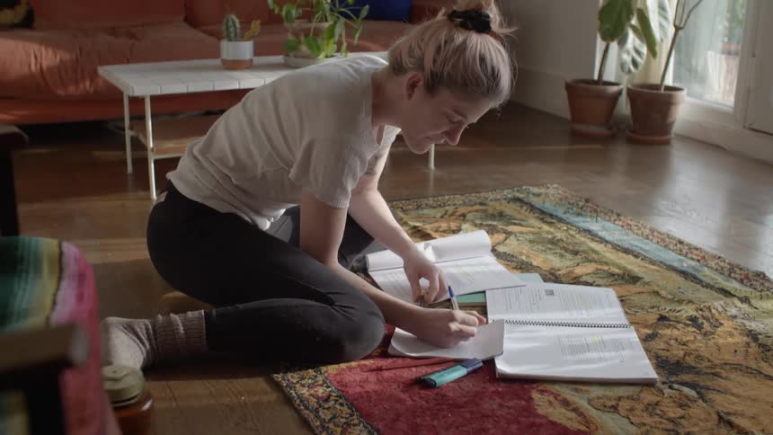 Young woman sitting over a rug in the floor of the livingroom studying