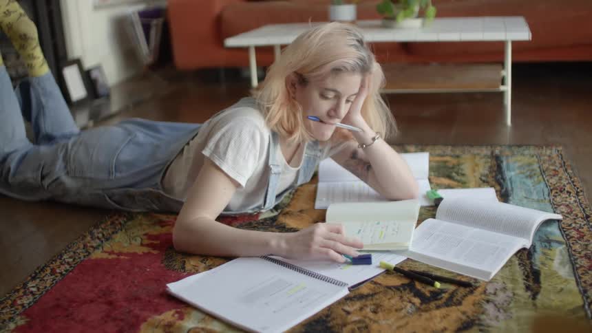 A woman laying on the floor on a rug writing on a book with a pen