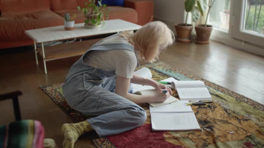 A woman in a room on the floor on a rug writing in a book
