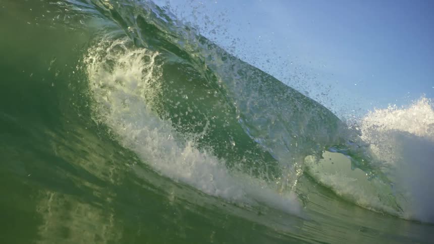 A ocean wave crashes as it rolls in towards the shore