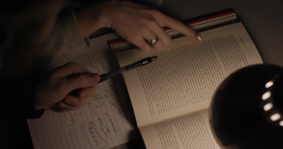 Two people taking notes from a book on a table under a table lamp at night