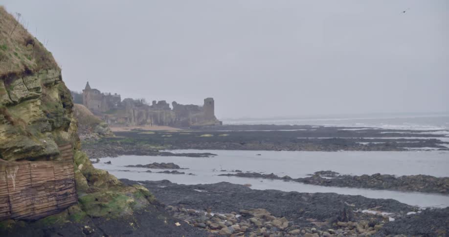 Ruins of a castle over a cliff in the horizon next to the ocean on an overcast day