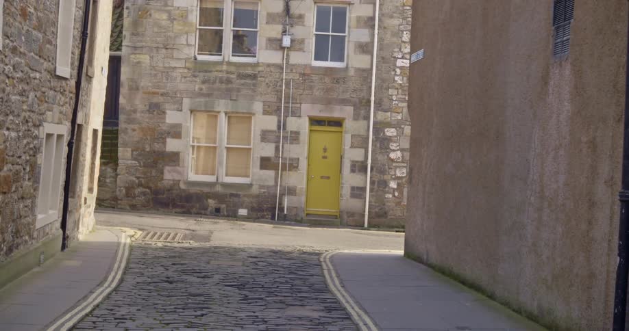 Narrow cobblestone road shadowed by buildings intersects with road