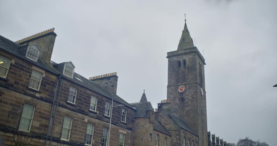 A building and clock tower in brown bricks against a gray sky