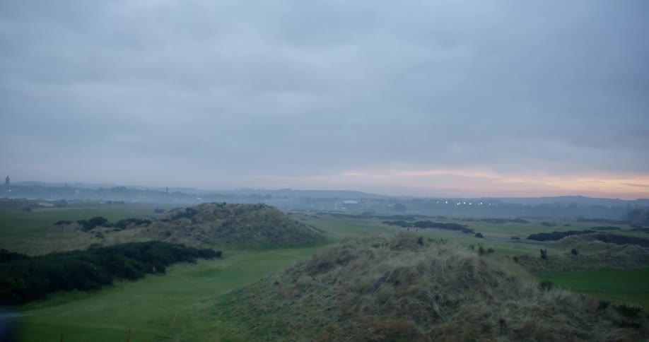 A green and hilly countryside under a cloudy evening sky