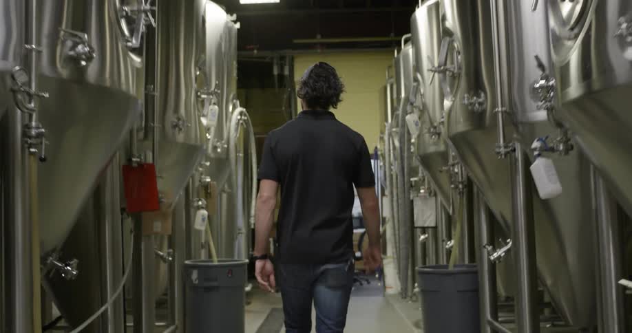 A brewery worker walks along a row of fermentation tanks in a distillery