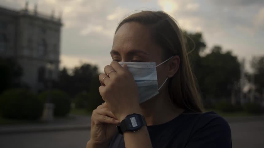 A woman on a city street puts a mask on