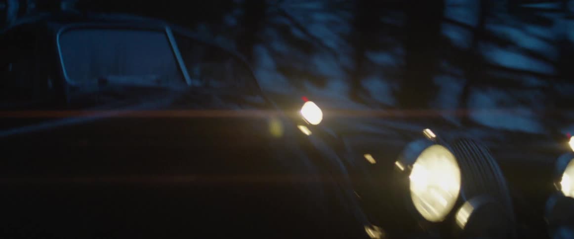 A car drives on a road with trees and snow on the side of the road