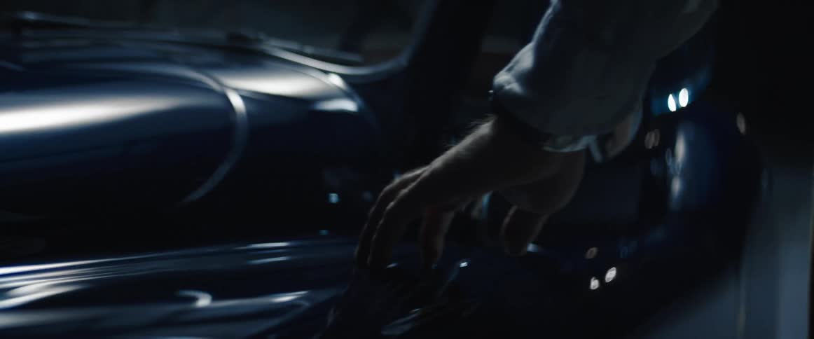 A man walking alongside a vintage car touching it with his hand at night