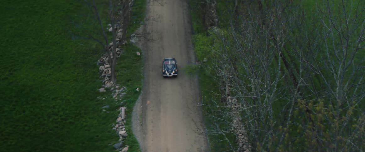 A car drives down a dirt road in a rural area