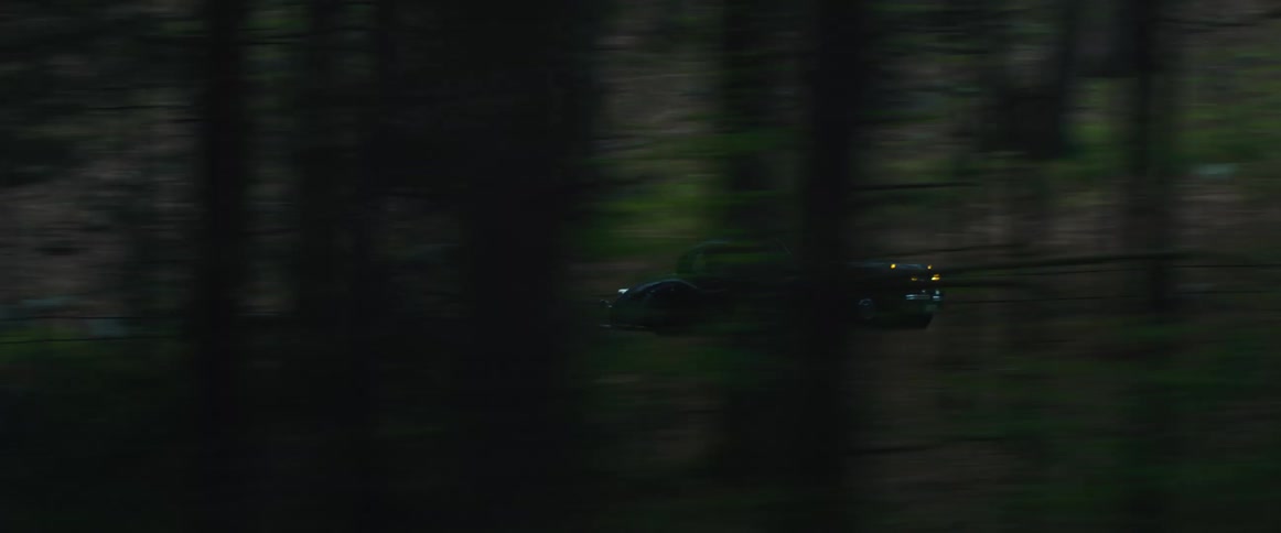 A sportscar and van drive down a paved road in a rural forested areas